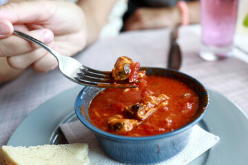 Person eating mussels in tomato sauce