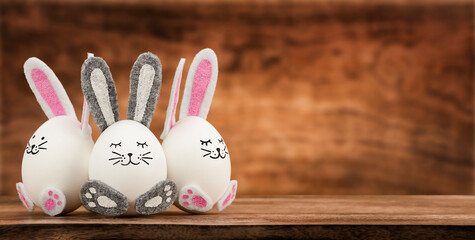 Three Easter eggs with bunny ears on wooden background with copy space. Easter concept