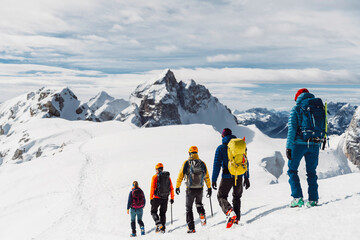 View from the back, five mountaineers descending down the snowy mountain, walking in a row 