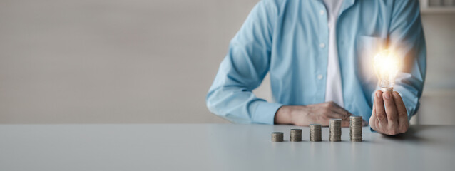 Businessman holds a glowing light bulb on top of the highest pile of coins, Placing coins in a row from low to high is comparable to saving money to grow more. Money saving ideas for investing in fund