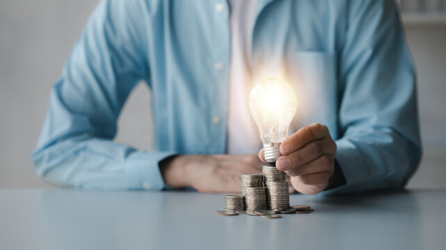 Businessman holds a glowing light bulb on top of the highest pile of coins, Placing coins in a row from low to high is comparable to saving money to grow more. Money saving ideas for investing in fund