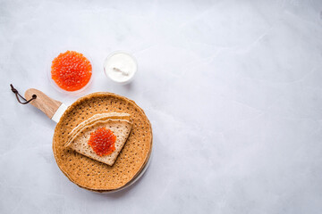 Russian traditions. Broad Maslenitsa. A stack of pancakes, sour cream and red caviar on a light background. Close-up.
