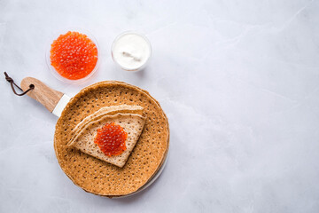Russian traditions. Broad Maslenitsa. A stack of pancakes, sour cream and red caviar on a light background. Close-up.