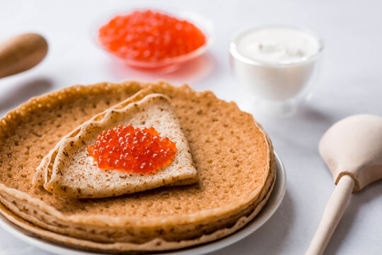 Russian traditions. Broad Maslenitsa. A stack of pancakes, sour cream and red caviar on a light background. Close-up.