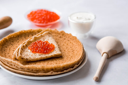 Russian traditions. Broad Maslenitsa. A stack of pancakes, sour cream and red caviar on a light background. Close-up.