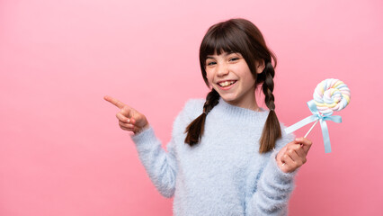 Little caucasian girl holding a lollipop pointing finger to the side