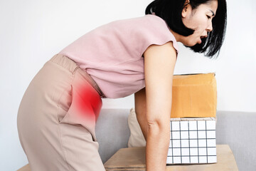 Asian woman suffering from abdominal pain or stomach muscle pain after incorrect lifting heavy boxes