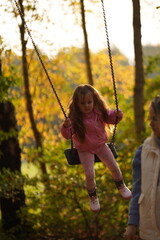 Young girl swinging on swing on an oak branch in sun. Dreams of flying. Happy childhood concept. Beautiful girl in park. Teen girl enjoys flight on swing on a summer evening in forest