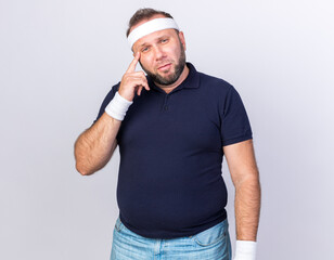thoughtful adult slavic sporty man wearing headband and wristbands putting finger on temple and...