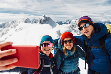 Woman hiker taking a selfie of the group while on top of the mountain on a sunny winter day