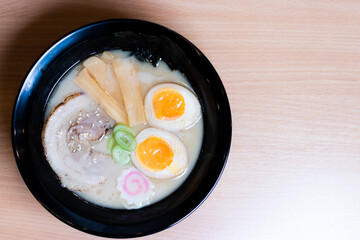 Tonkotsu ramen in a black cup topped with chashu pork, Naruto fish balls, soy-sauce pickled eggs, menma bamboo shoots and seaweed. Ramen is a distinctive Japanese style noodle soup.