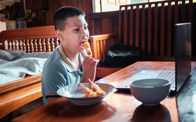 Asian boys eat junk food while sitting at a desk with notebooks, and laptops at home