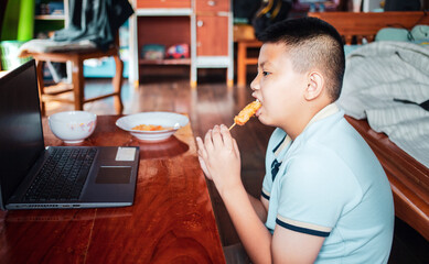 Asian boys eat junk food while sitting at a desk with notebooks, and laptops at home