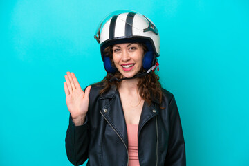 Young caucasian woman with a motorcycle helmet isolated on blue background saluting with hand with happy expression