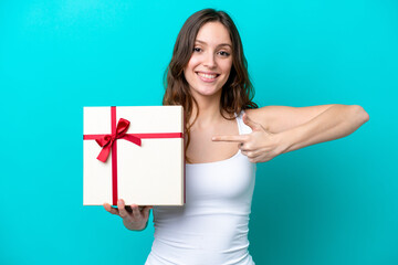 Young caucasian woman holding a gift isolated on blue background and pointing it