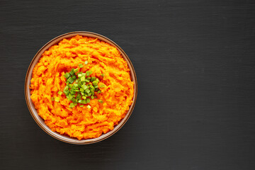 Homemade Creamy Mashed Sweet Potatoes with MIlk and Butter in a Bowl on a black background, top view. Space for text.