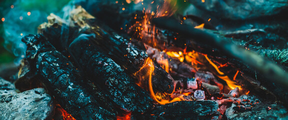 Fototapeta na wymiar Vivid smoldered firewoods burned in fire close-up. Atmospheric warm background with orange flame of campfire and blue smoke. Full frame image of bonfire. Beautiful whirlwind of embers and ashes in air