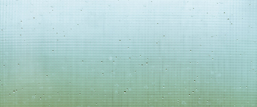 Mosquito net on wet window with rainy drops and dirt spots closeup. Rain droplets on glass with mosquito screen. Blurry minimal background with greenery bokeh against dirty window glass with raindrops