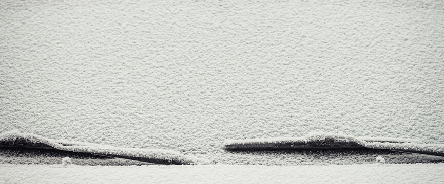 Minimalist nature background with white snow on flat surface. Snow-covered frozen windshield. Minimal winter backdrop with snowbound glass of car close up. Natural large snow grains on windscreen.