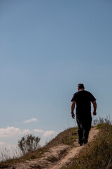 Man dressed in black walking on a path on a cliff where you can see the blue sky