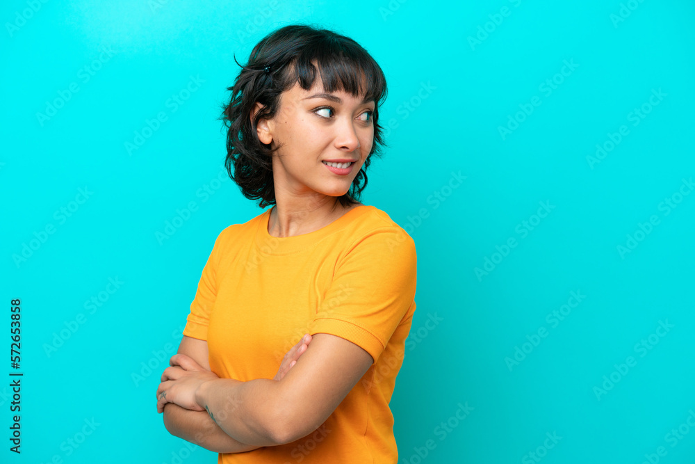 Wall mural young argentinian woman isolated on blue background looking to the side and smiling