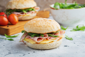 Two homemade sandwiches with ham, cheese and arugula on a concrete table.