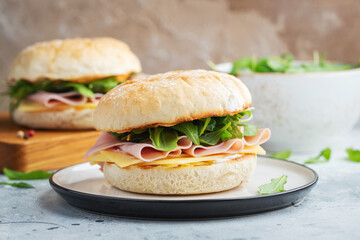 Two homemade sandwiches with ham, cheese and arugula on a concrete table.