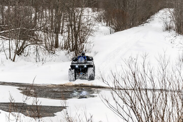 A man driving his ATV across the river in the wilderness at winter.