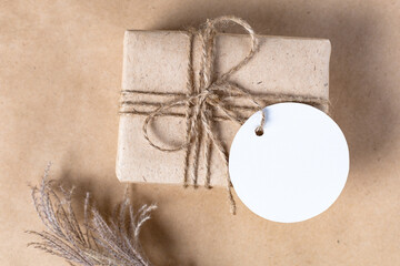 empty white gift tag mock up on craft paper box with dried spikelets decoration on natural beige...