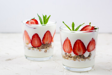 White yogurt with fresh strawberries granola and mint in two glasses on a white background.