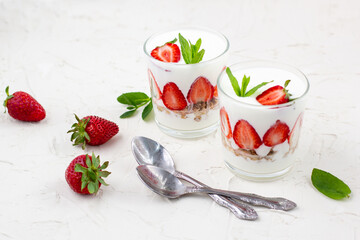 White yogurt with fresh strawberries granola and mint in two glasses on a white background.
