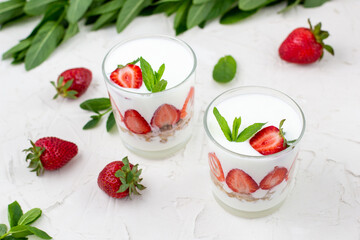 White yogurt with fresh strawberries granola and mint in two glasses on a white background.