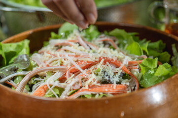 Hand chef sprinkle parmesan cheese shredded on caesar salad in wood blow. Caesar salad or green salad in wood blow must sprinkle by parmesan cheese shredded. parmesan cheese shredded is mix in Italian