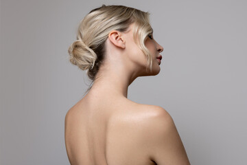Young beautiful woman stands on her side with bare shoulders and back. Concept of hair and makeup,...