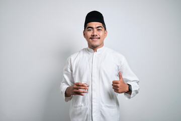 Asian muslim man in white prayer clotes smiling and thumbs up while going to drink a glass of water...