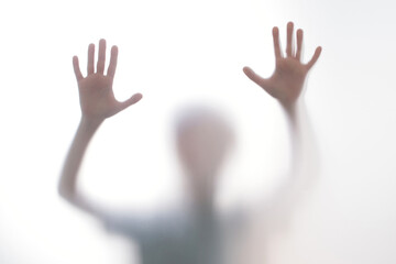 Silhouette scared boy stand behind glass door. Kid showing two hands.