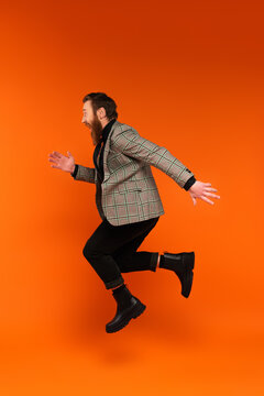 Side view of excited stylish man jumping on red background.