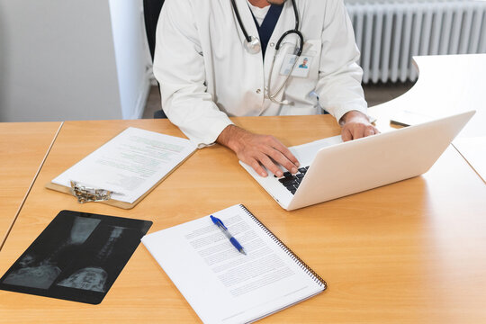 Focused anonymous doctor working on laptop