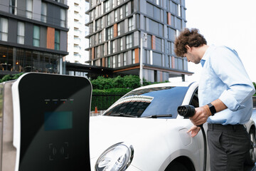 Progressive businessman insert charger plug from charging station to his electric vehicle with...