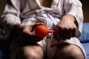 Constipation concept. An unrecognizable man in a bathrobe holds an enema in his hands. Disorder of...