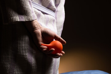 Constipation concept. An unrecognizable man in a bathrobe holds an enema in his hands. Disorder of...