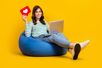 Full size photo of good mood positive cute woman striped sit on armchair hold laptop like heart isolated on yellow color background - Powered by Adobe