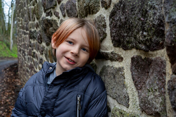 Smiling contented boy near the stone wall looks at the camera. A boy of nine and ten years of age...