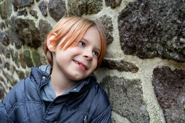 Smiling contented boy near the stone wall. A boy of nine and ten years of age with long red hair....