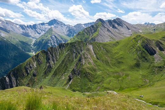 A panoramic view of the Samnaun Alps with the highest peaks visible in the distance. The photo was taken from the Alp Trida Sattel in Austria. In the foreground the green grass with a small stream. 