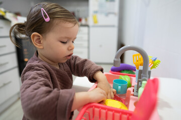 One little toddler girl playing in the kitchen with her toy dishwasher, early child development...