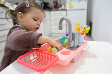 One little toddler girl playing in the kitchen with her toy dishwasher, early child development concept