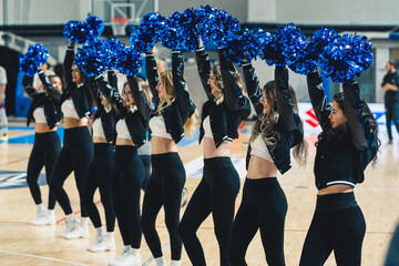 pretty cheerleaders in black pants and jackets and white tops holding blue pom-poms up. High quality photo