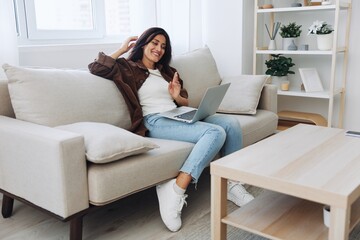 Woman freelancer on her day off sitting on the couch with a laptop at home and watching series and tv shows, smile