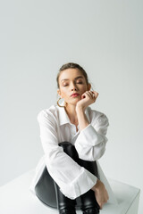 stylish woman in white shirt and black tight pants sitting with closed eyes isolated on grey.